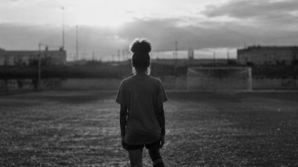 Joueuse de football de dos sur un terrain au coucher du soleil en noir et blanc, illustrant l'article sur les femmes dans le sport – Hystérie Collective