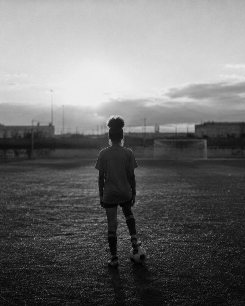 Joueuse de football de dos sur un terrain au coucher du soleil en noir et blanc, illustrant l'article sur les femmes dans le sport – Hystérie Collective