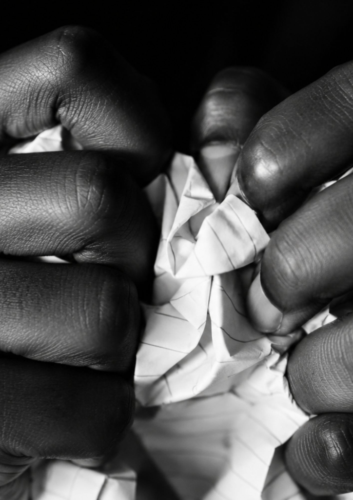 Mains froissant un papier en noir et blanc, illustrant l'article sur la liste humiliante de classement de jeunes filles créée par des hommes sur les réseaux sociaux – Hystérie Collective